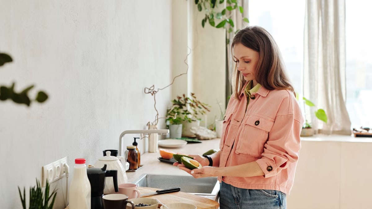 Woman preparing avocado in a modern kitchen with natural light.